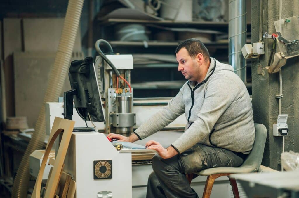 Factory worker operating drilling cnc machine at wood machining industry